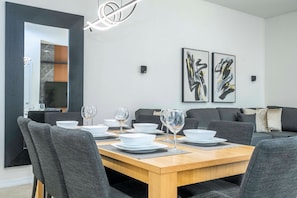 A modern dining area with a wooden table set for two, surrounded by grey upholstered chairs. - 3BR themed rooms near Disney | Private hot tub (Kissimmee)