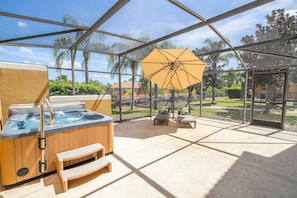 A covered outdoor area with a hot tub, seating, and an umbrella. - 3BR themed rooms near Disney | Private hot tub (Kissimmee)