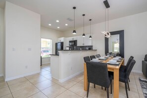 A modern kitchen with a central island, overhead pendant lighting, and a dining area with a wooden table and chairs. - 3BR themed rooms near Disney | Private hot tub (Kissimmee)
