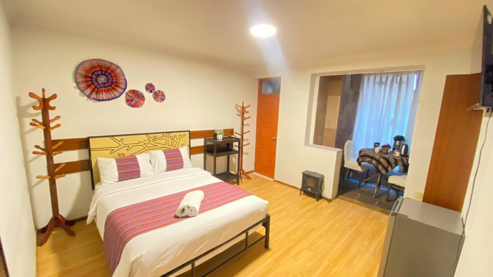 Une chambre d’hôtel avec un lit, une petite table, une chaise, une télévision et une fenêtre avec des rideaux.