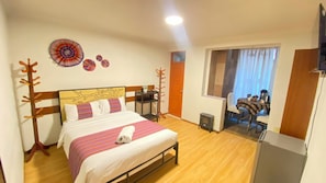 A hotel room with a bed, a small table, a chair, a TV, and a window with curtains.