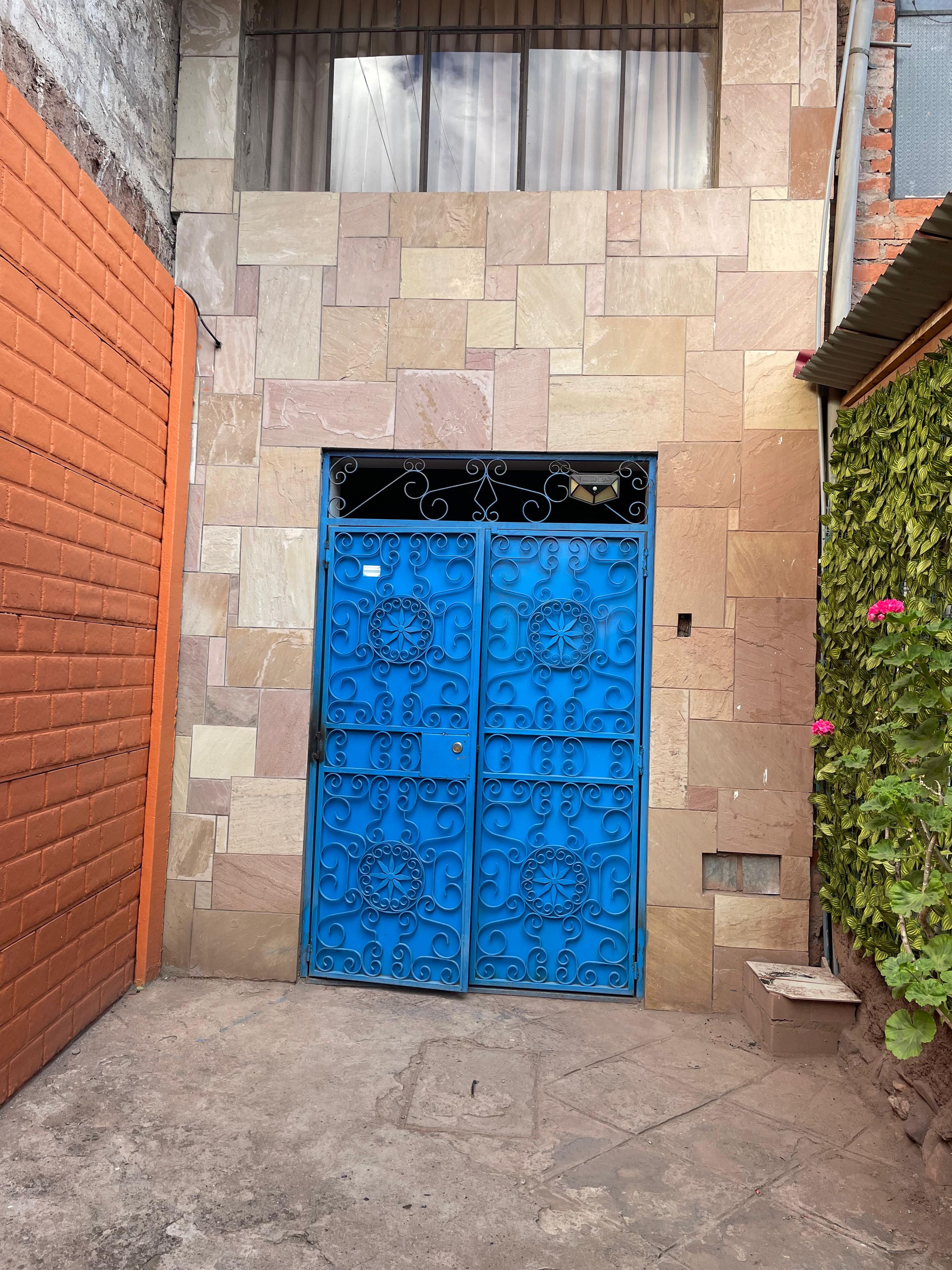 Une porte bleue ornée de motifs complexes, un mur de briques et un mur de pierres avec une fenêtre au-dessus.