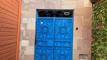 Une porte bleue ornée de motifs complexes, un mur de briques et un mur de pierres avec une fenêtre au-dessus.