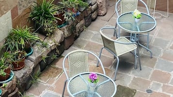 Une terrasse avec un sol en pierre, des chaises et des tables en métal, entourée de plantes en pot.