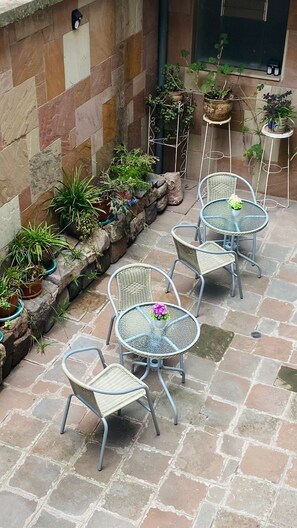 Une terrasse avec un sol en pierre, des chaises et des tables en métal, entourée de plantes en pot.