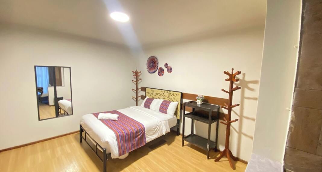 Een slaapkamer met een bed, nachtkastje, spiegel en een kapstok aan de muur.