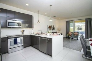 A modern kitchen with a central island, built-in appliances, and a dining area with a view. - 3BR near Disney | Mickey room, private pool (Clermont)
