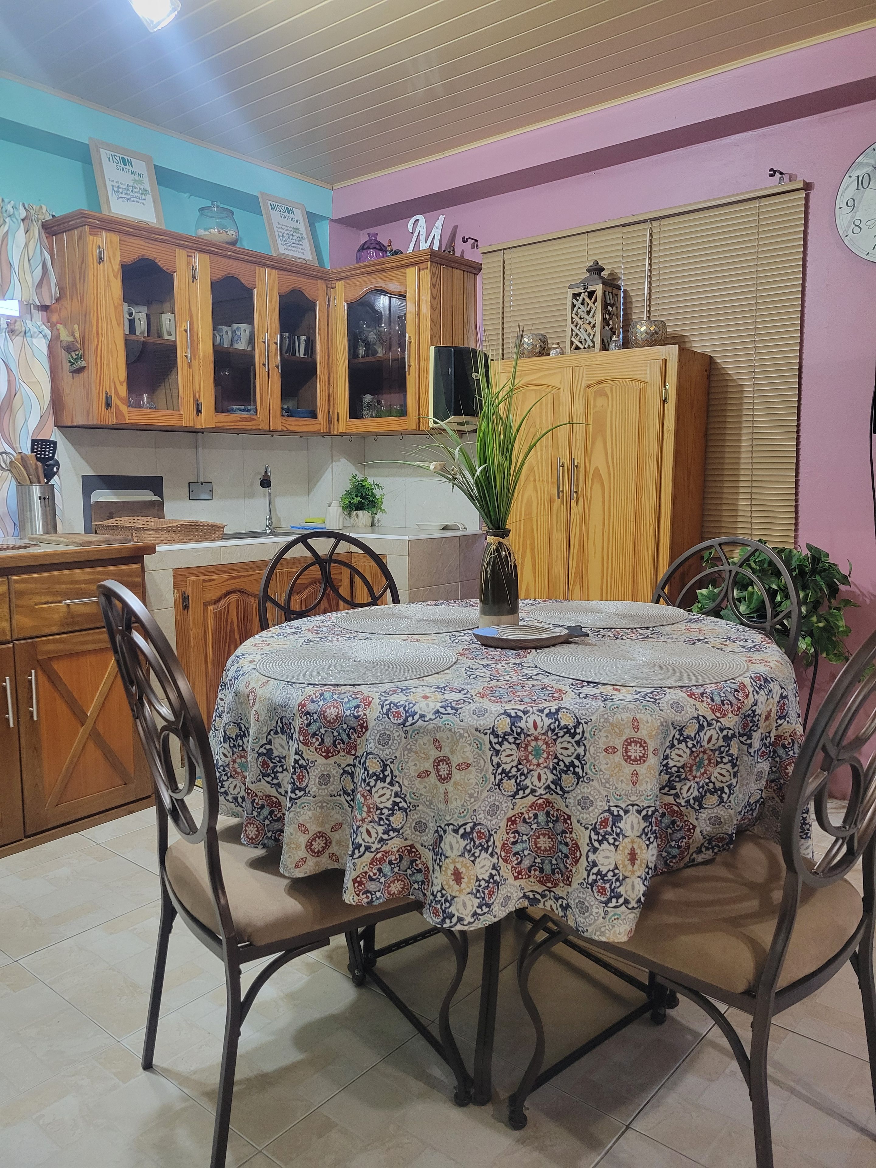 Un comedor con una mesa redonda cubierta por un mantel estampado, rodeado de sillas.