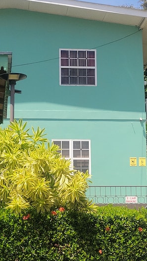 A two-story building with a green exterior, two windows, and a '2 car parking' sign. - Matty's Inn (Mayaro)