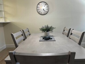 Ein Esstisch mit sechs Stühlen, eine Uhr an der Wand und eine Zimmerpflanze in der Mitte.