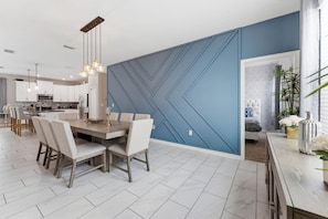 A modern kitchen with white cabinets, a dining area with a wooden table and chairs, and a blue accent wall. - 4BR themed home ChampionsGate | Pool & spa (Davenport)