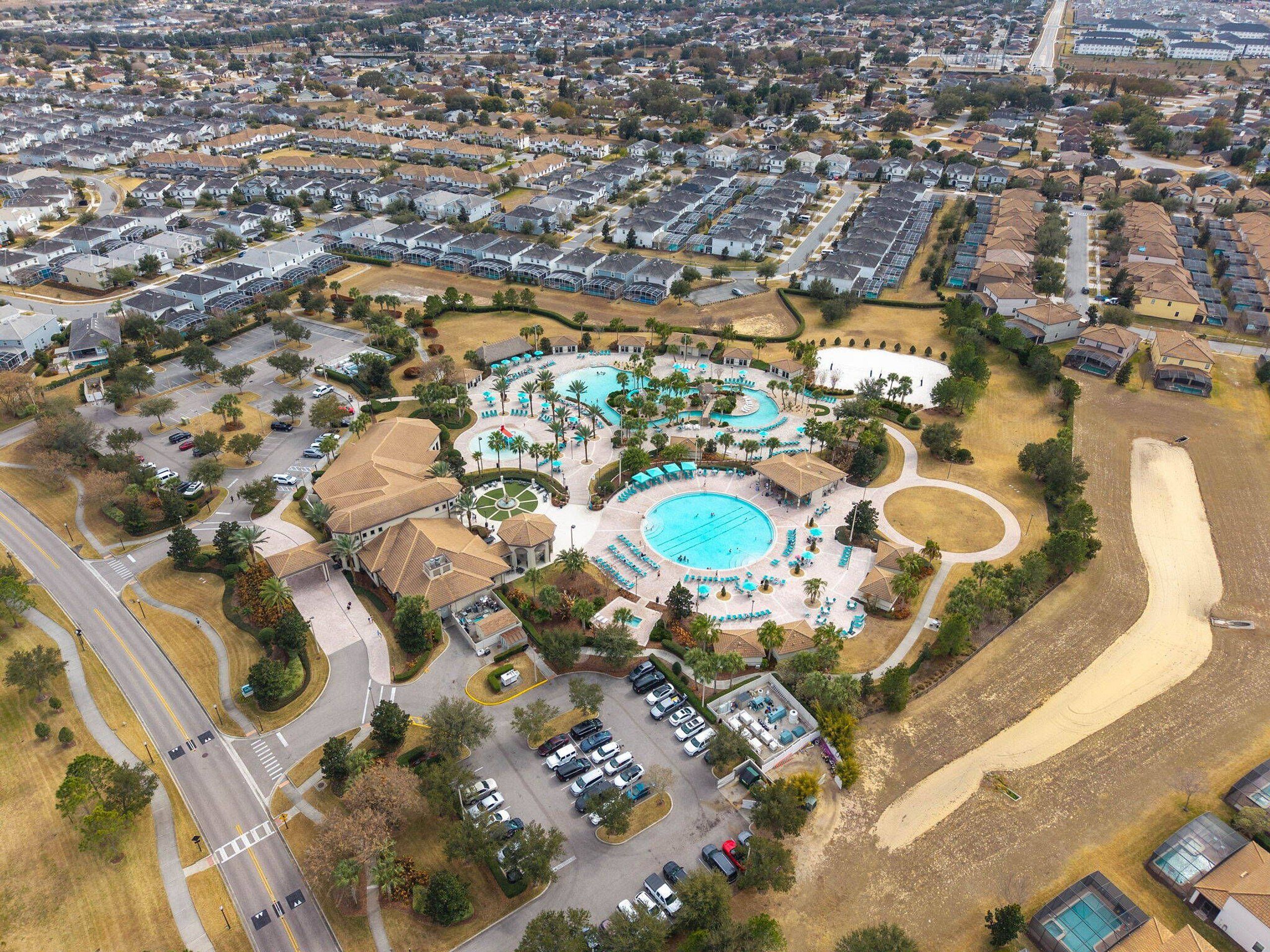 An aerial view of a residential area with a swimming pool complex, parking, and a road.