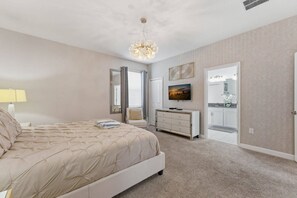 Une chambre à coucher avec un lit, une commode, un téléviseur et une porte menant à la salle de bain.