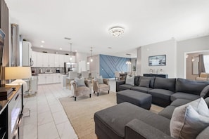 A modern living room with a grey sectional sofa, a coffee table, and a dining area with chairs. - 4BR themed home ChampionsGate | Pool & spa (Davenport)