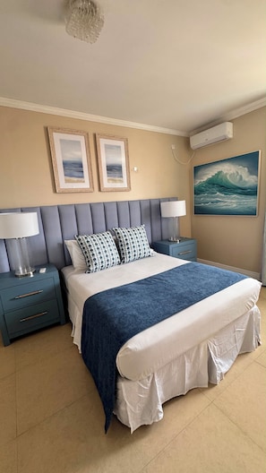 A hotel room with a bed, two nightstands, a wall-mounted air conditioner, and framed artwork. - Oleander Villa by Bay Gardens Resorts (Gros Islet)