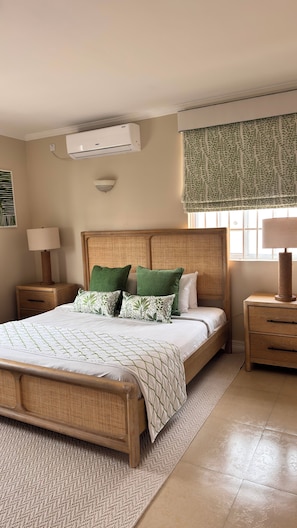 Ein Schlafzimmer mit einem Bett, Nachttischen, einer Lampe, einer Klimaanlage und einem Fenster mit einem gemusterten Vorhang.