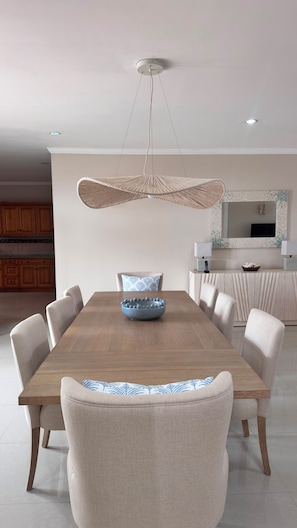 Un coin repas avec une table en bois, six chaises, un luminaire suspendu et une cuisine en arrière-plan.