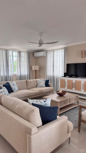 Ein modernes Wohnzimmer mit einem beigen Sofa, einem Couchtisch, einem Fernseher und einem Deckenventilator.