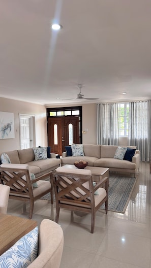 A spacious living room with a large sectional sofa, a wooden coffee table, and a dining area with a wooden chair. - Oleander Villa by Bay Gardens Resorts (Gros Islet)