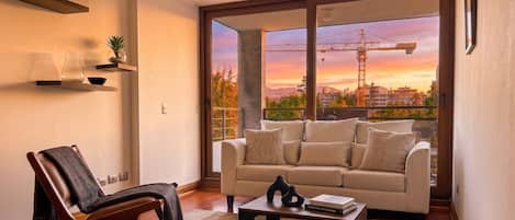 A living room with a sofa, armchair, coffee table, and a view of a construction site through a large window.