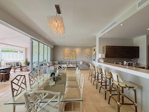 A modern living room with a glass coffee table, a sofa, and a dining area with chairs. - Breeze & Lake 4BR House in Puntarena (Río Hato)