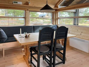 Interior acogedor de una cabaña con una mesa de madera, dos sillas, un banco y ventanas amplias que ofrecen vistas al exterior.