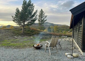 A gravel patio with a fire pit, two chairs, and a building with large windows.