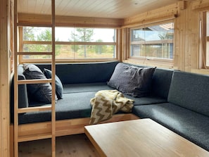 A cozy cabin interior with a built-in bench and a table, large windows offering a view of trees, and wooden walls.