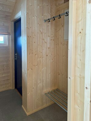 Un interior de madera con una puerta, un perchero metálico y una ventana.