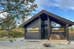 A cabin with a sloped roof, large windows, and a deck area with a fire pit.