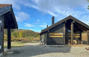 A cabin with a gravel driveway, wooden deck, and a view of a mountainous landscape.