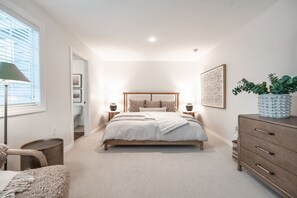 Een slaapkamer met een bed, nachtkastjes, een kast, een lamp, een plant en een raam met jaloezieën.