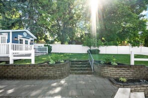 A backyard with a wooden deck, a white fence, and a brick planter with plants. - Downtown CDA Guest House | Walk to Beach & Tubb’s (Coeur d`Alene)