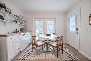 A compact kitchen with white cabinetry, a round dining table, and a striped rug. - Downtown CDA Guest House | Walk to Beach & Tubb’s (Coeur d`Alene)