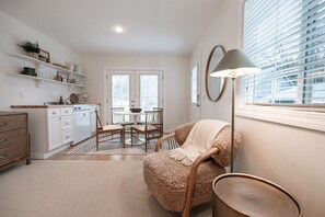 A modern kitchen with white cabinetry, a dining area with a round table and chairs, a fluffy armchair, and a floor lamp. - Downtown CDA Guest House | Walk to Beach & Tubb’s (Coeur d`Alene)