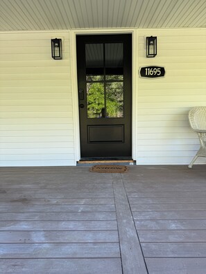 A house with a dark front door, a welcome mat, and a number sign above the door. - Cozy 2-bedroom cottage in charming Linesville with AC (Linesville)