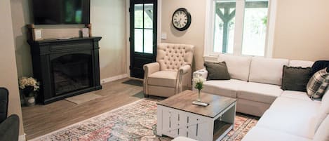 A living room with a fireplace, a television, a sofa, a chair, and a clock on the wall.
