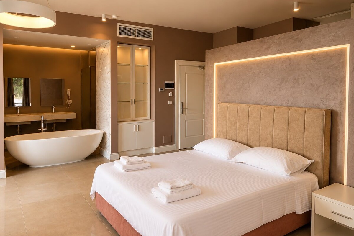 A modern bedroom with a large bed, bedside tables, a built-in headboard, and a separate bathroom with a bathtub and vanity.