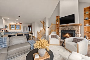 A modern living room with a fireplace, a sofa set, a dining area, and a kitchen in the background. - Tremblant Prestige - Clairière 403 (Mont-Tremblant)
