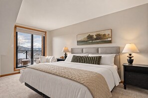 A bedroom with a large bed, two bedside tables, a window with a view, and a painting on the wall. - Tremblant Prestige - Clairière 403 (Mont-Tremblant)