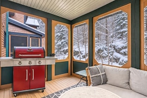 A cozy room with a red grill, a cushioned sofa, and large windows with a snowy forest view. - Tremblant Prestige - Clairière 403 (Mont-Tremblant)
