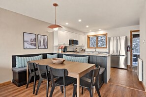 A modern kitchen with a dining area, featuring a wooden table, black chairs, and a large island with seating. - Tremblant Prestige - Clairière 403 (Mont-Tremblant)