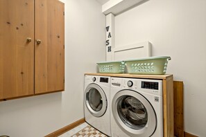 A laundry room with two front-loading washing machines, wooden cabinets, and a wall-mounted sign that reads 'WASH'. - Tremblant Prestige - Clairière 403 (Mont-Tremblant)