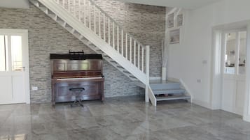 A spacious living area with a piano, a staircase, and a door leading to another room.