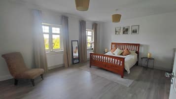 A bedroom with a wooden bed, a chair, a mirror, and a window with curtains.