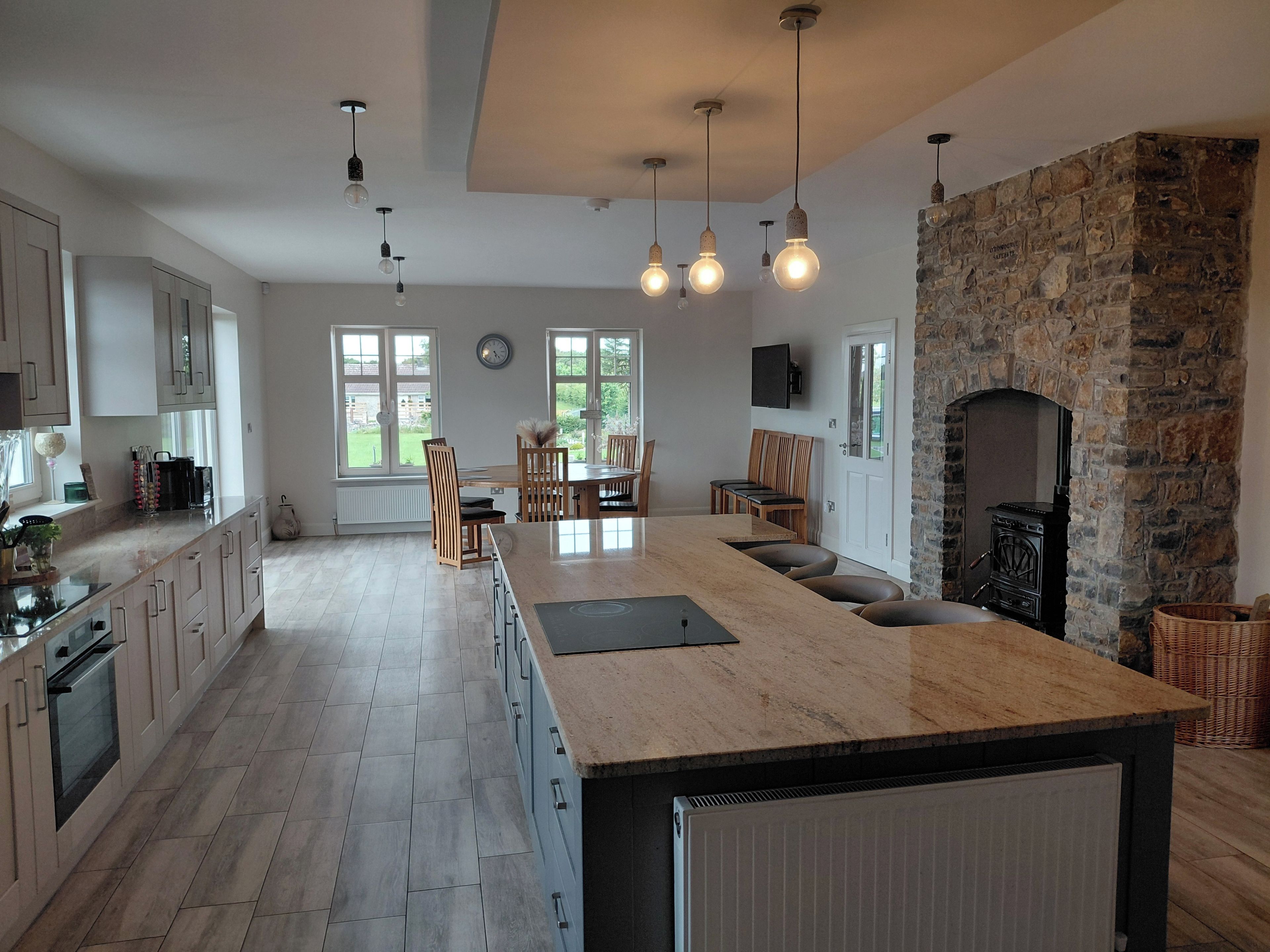 A modern kitchen with a large island, stone fireplace, and dining area with natural light.