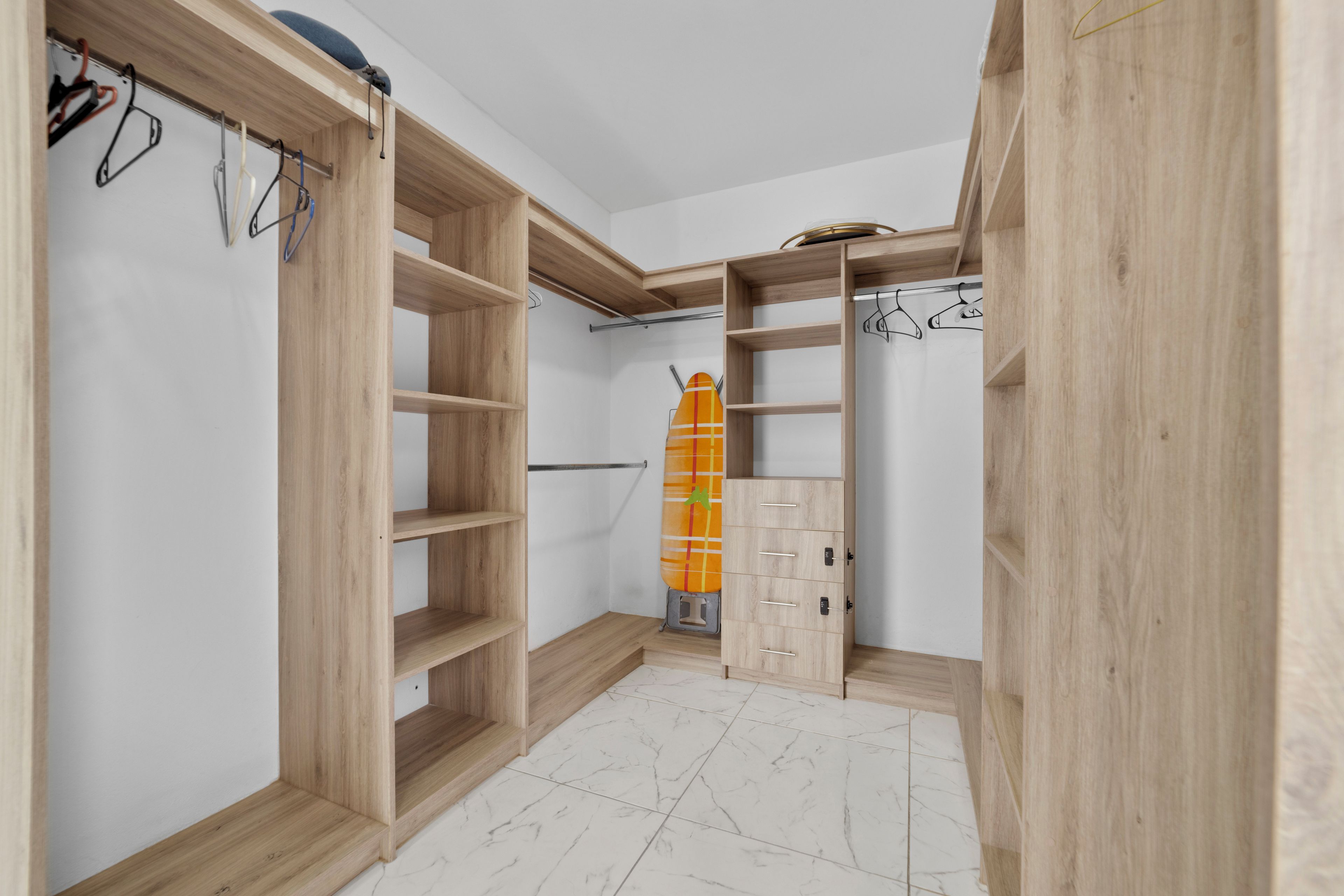 A walk-in closet with open shelving and a hanging rod, featuring a tiled floor and a wooden ceiling.
