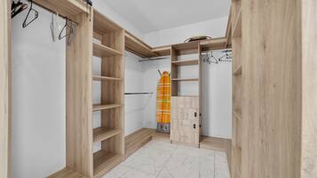 A walk-in closet with open shelving and a hanging rod, featuring a tiled floor and a wooden ceiling.