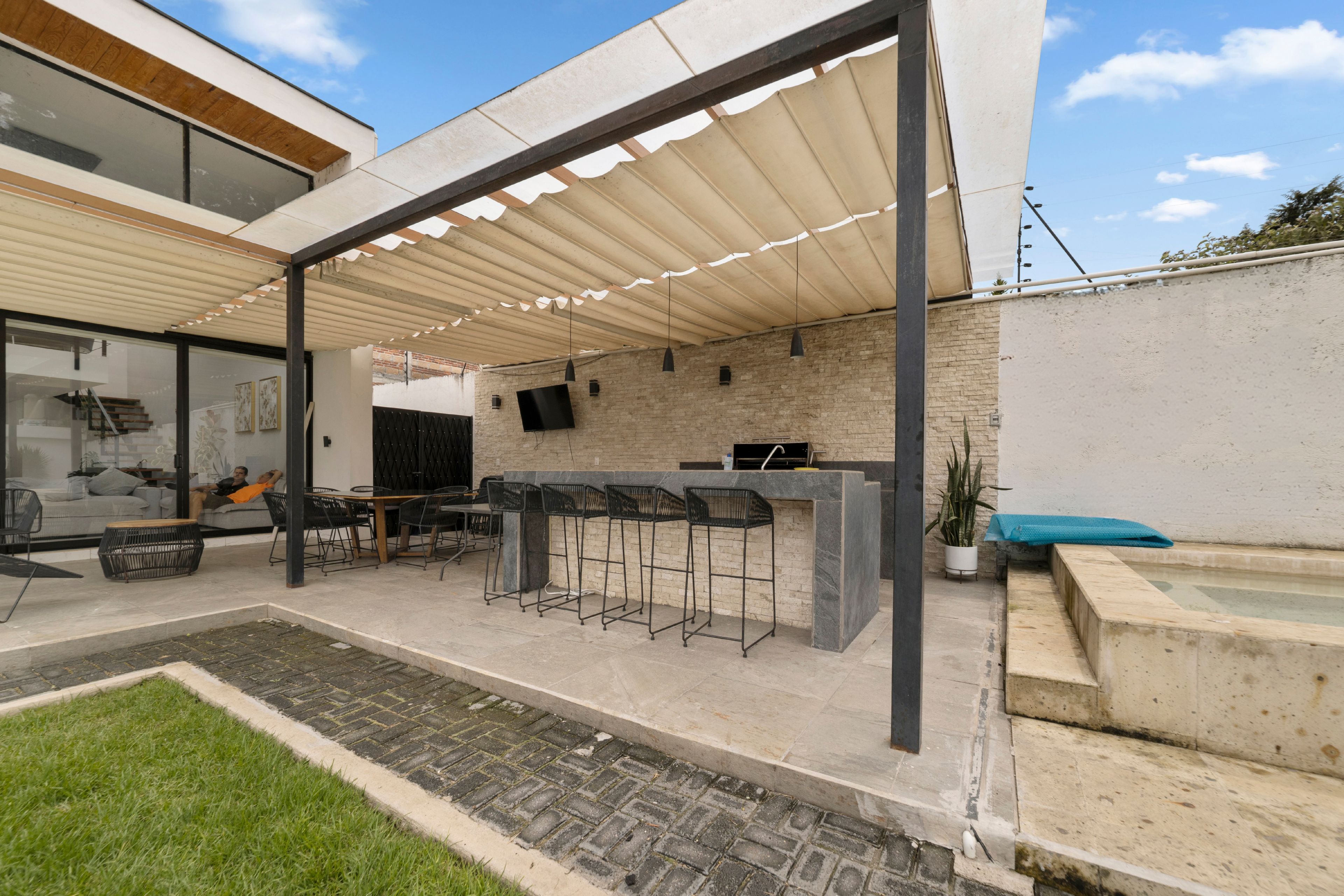 An outdoor patio area with a covered seating area, a bar counter, and a pool.