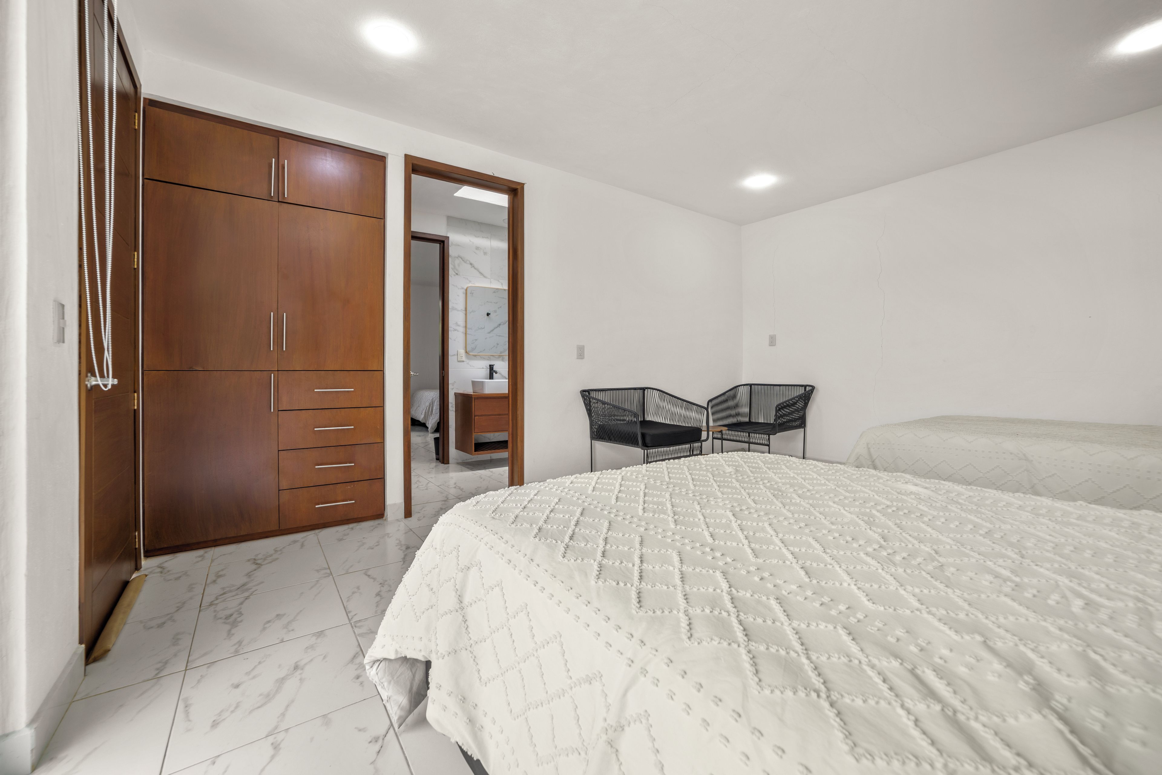 A bedroom with a large bed, a wardrobe, a mirror, and two chairs.